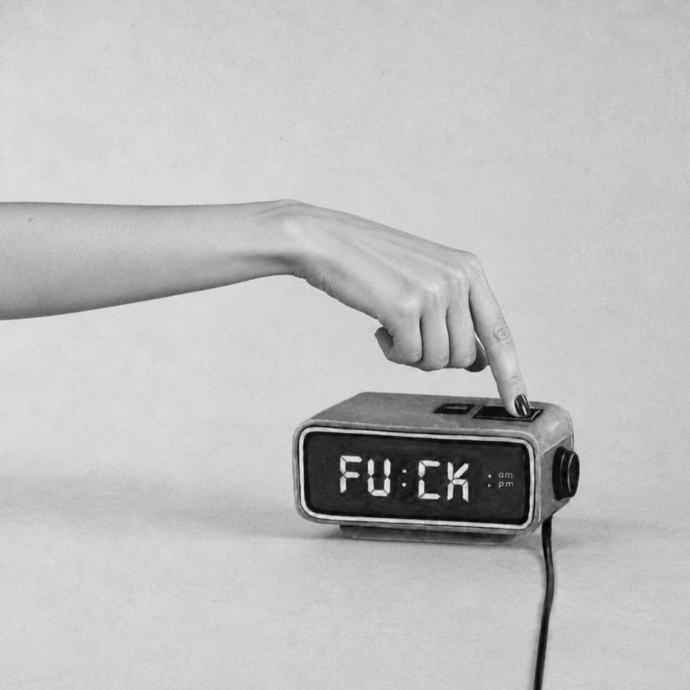 Black-and-white image of a woman pressing snooze on a digital alarm clock displaying “FUCK.”Black-and-white image of a woman pressing snooze on a digital alarm clock displaying “FUCK.”