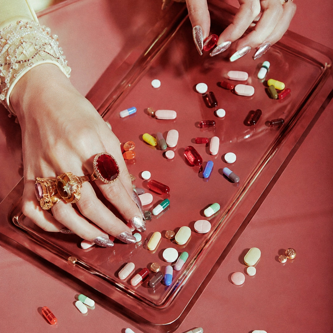 Jewelled hands sorting assorted pills on a red tray, representing the fragmented approach to perimenopause symptom support.